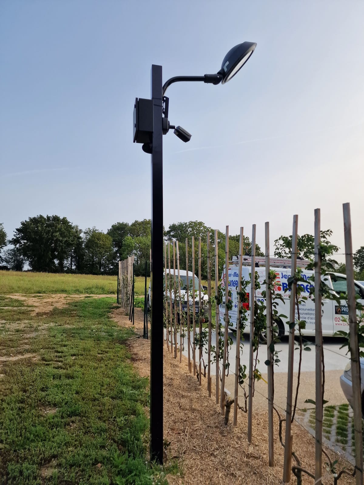 Mât avec caméra, éclairage et coffret de transmission en bordure de parking